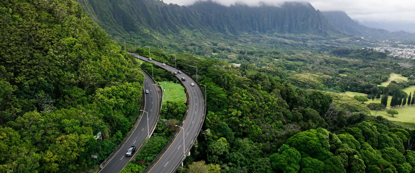 Aerial over a coastal highway winding through the green Oahu mountains